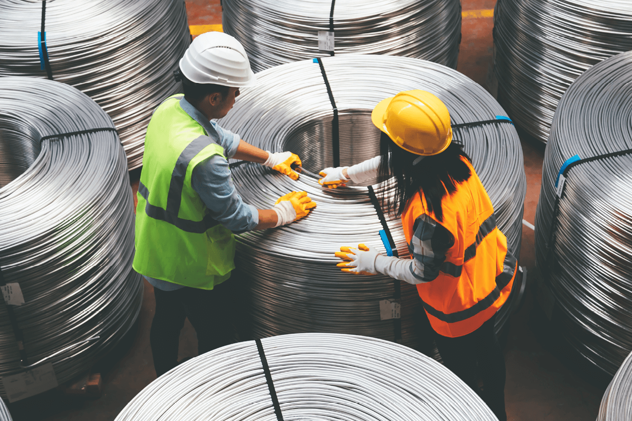 Two workers in safety gear inspecting large coil of tubing
