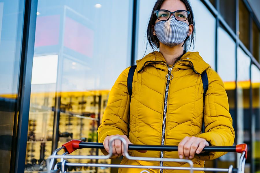 Masked woman outside a grocery store pushing a cart