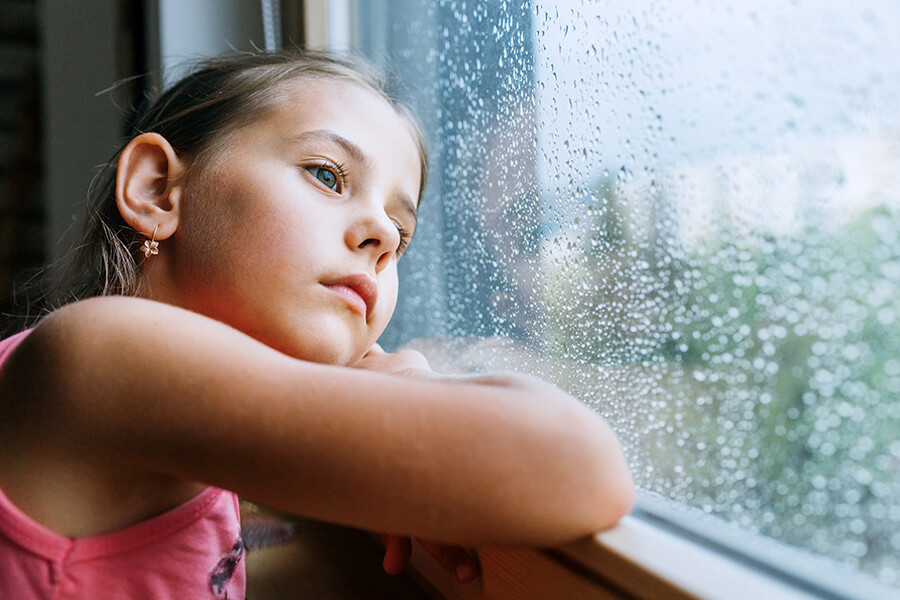 Young girl looking out a rain-splattered widnow