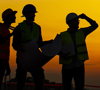 Three construction workers silhouetted against a sunset