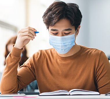 Masked student studying in classroom