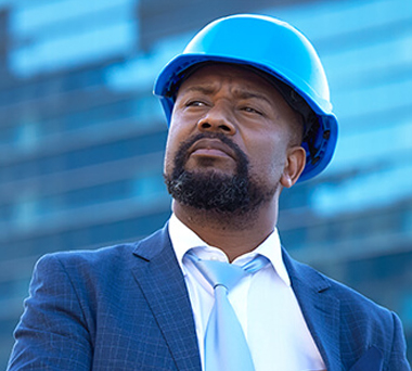 Black man in suit and hardhat in front of office building