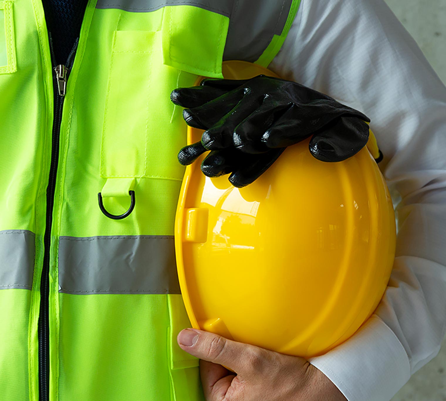 Close-up of worker in safety vest holding hard hat and safety gloves.