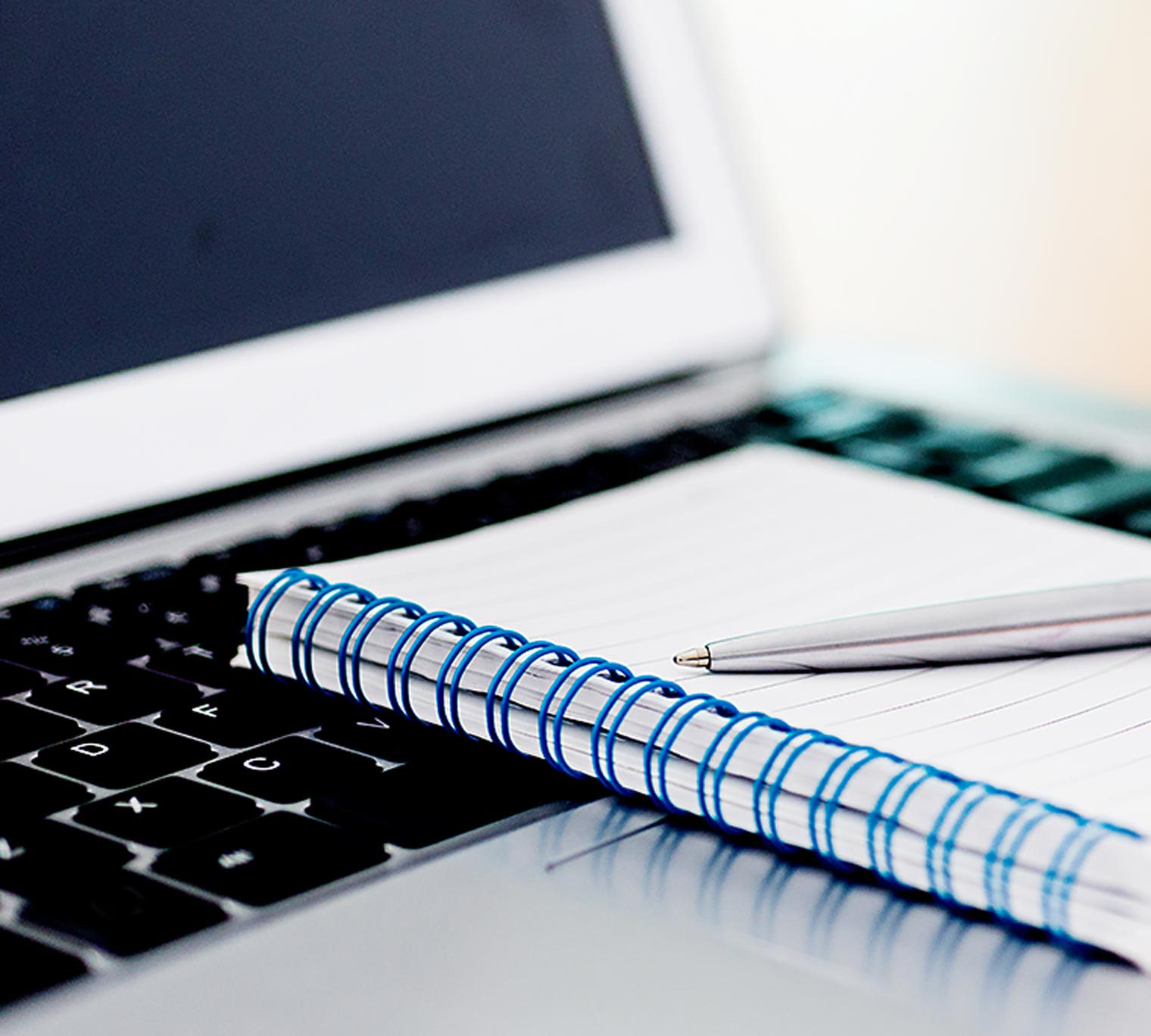Close-up of laptop with pen and spiral notebook.