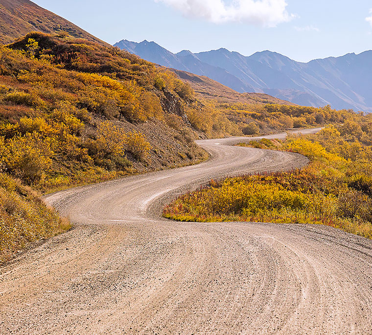 winding and bumpy dirt road with hills and mountains in the background