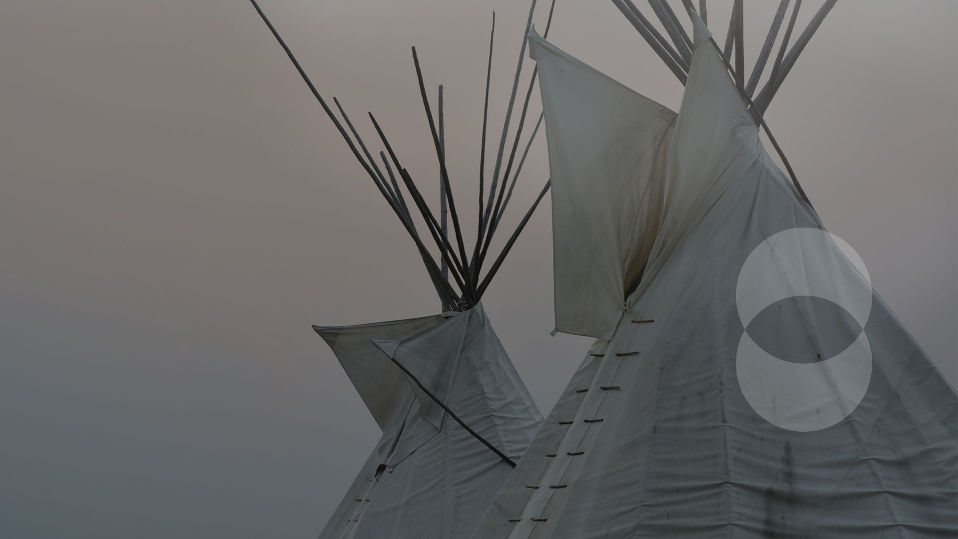 Two Indigenous conical shelters on a foggy sky backdrop