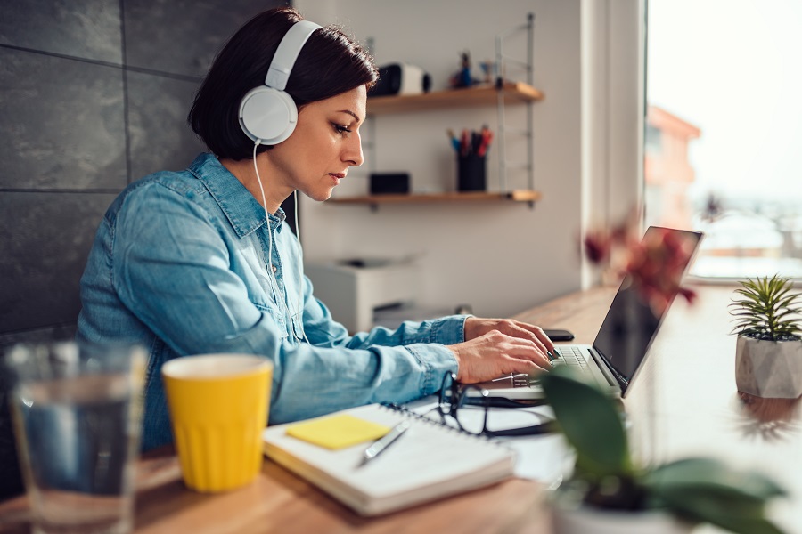 Business woman wearing denim shirt using laptop and listening music on a headphones