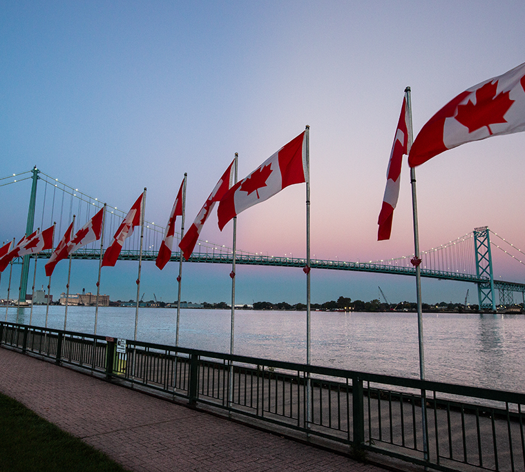 Canadian flags along a river with bridge in background
