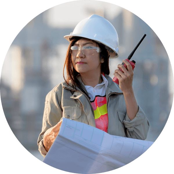 Indigenous woman wearing hard hat and holding two-way radio and blueprints