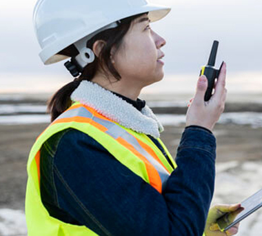 Woman working in a field wearing safety gear and with a walkie talkie