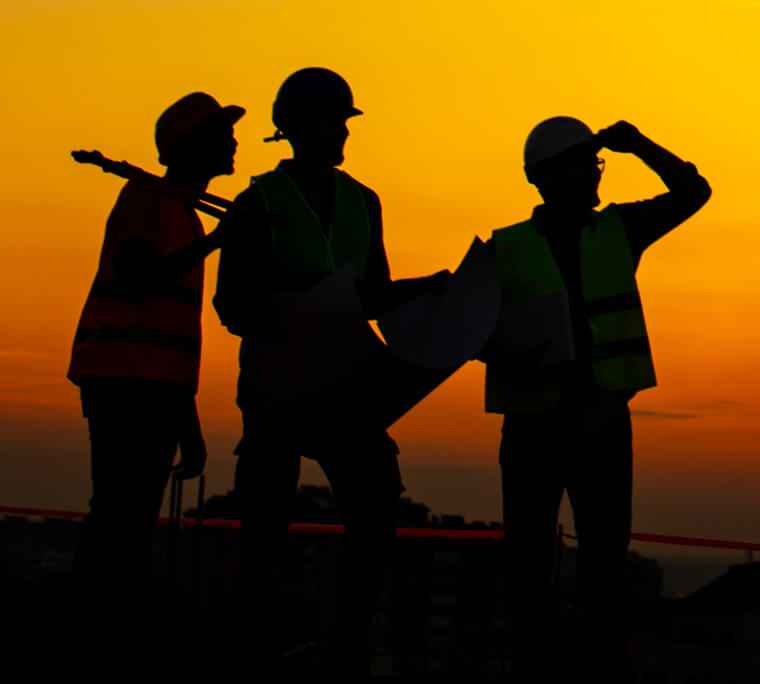 Three construction workers silhouetted against a sunset