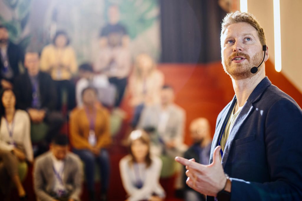Bearded white man turning to look at screen while presenting to an audience
