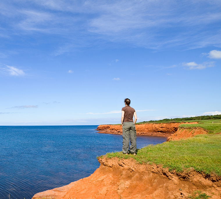person standing on edge overlooking the ocean with red sandy cliffs