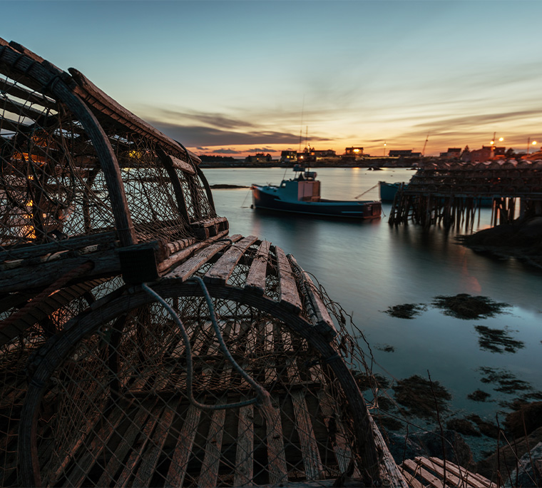 Wooden lobster traps are stacked on the wharf of a Nova Scotian fishing village in dusk light